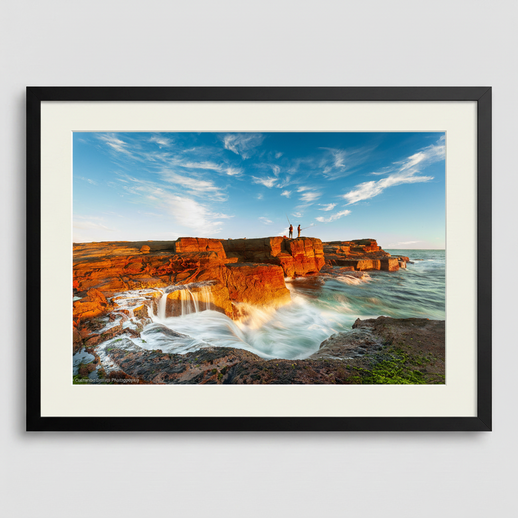 A landscape photograph featuring two figures fishing from a cliff edge with a vibrant sunset in the background, over a body of water. Norah Head lighthouse, NSW coast — fine art coastal wall art