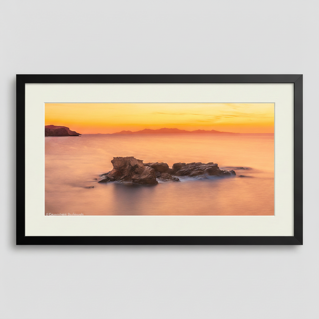 A photograph depicting a sunset over the Aegean Sea from Antiparos, Greece, with a rock formation in the foreground.