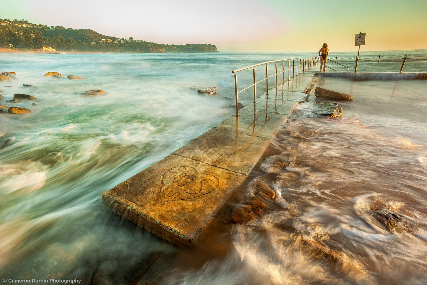 Person standing in Newport ocean pool at sunrise, Northern Beaches Sydney with soft golden light and calm water