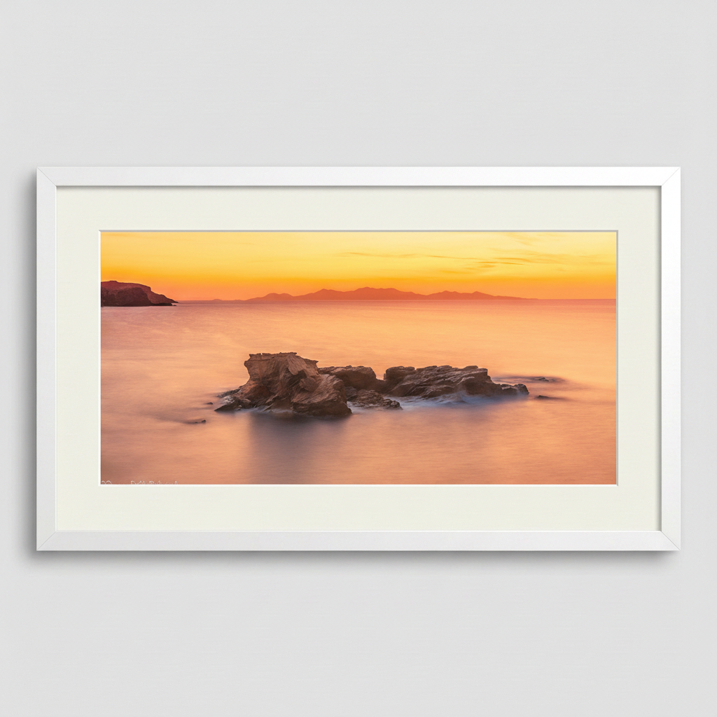 A photograph depicting a sunset over the Aegean Sea from Antiparos, Greece, with a rock formation in the foreground.